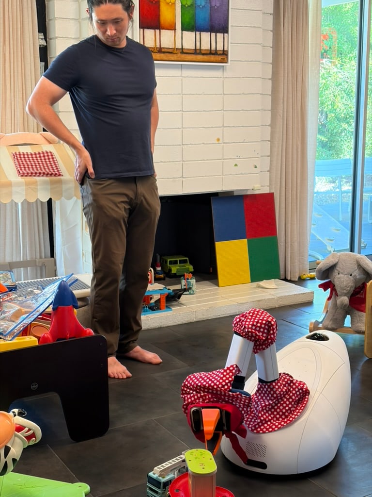 A person stands beside a Goose prototype among toys in a playroom.