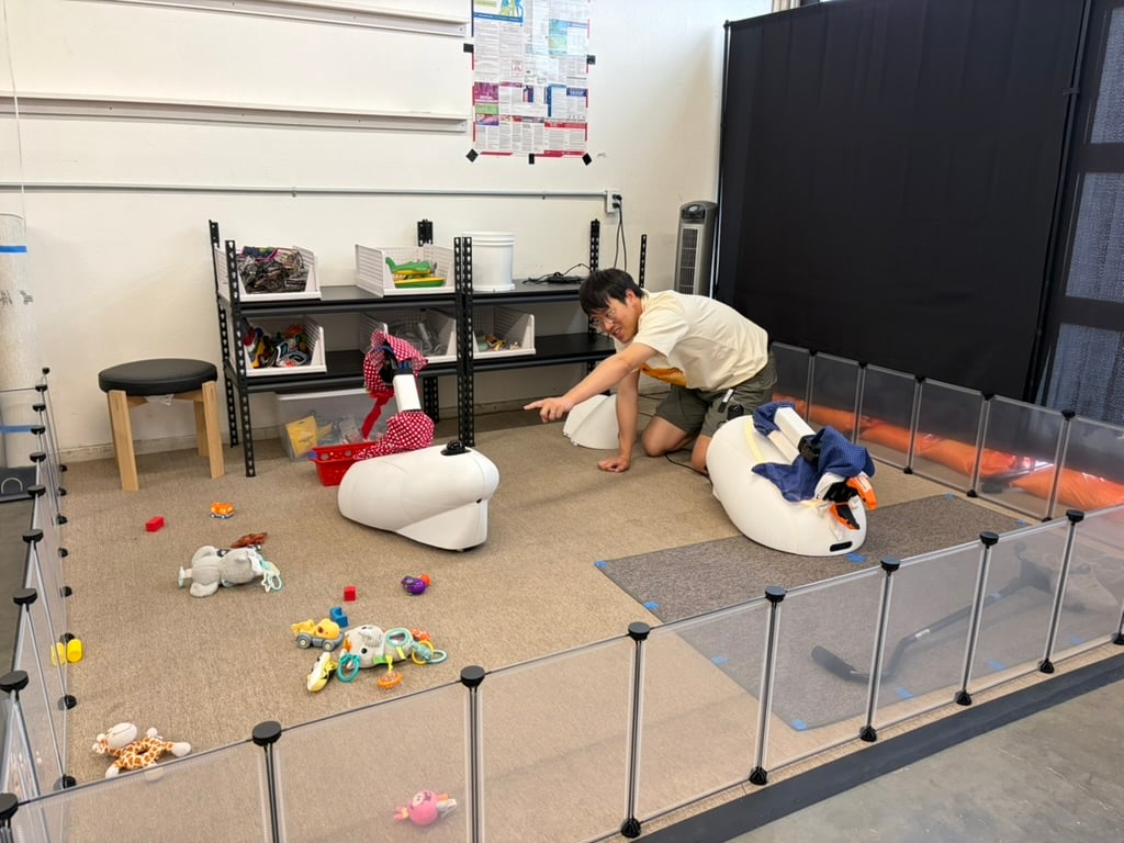 A person kneels beside two Goose prototypes and scattered toys inside a clear enclosure.