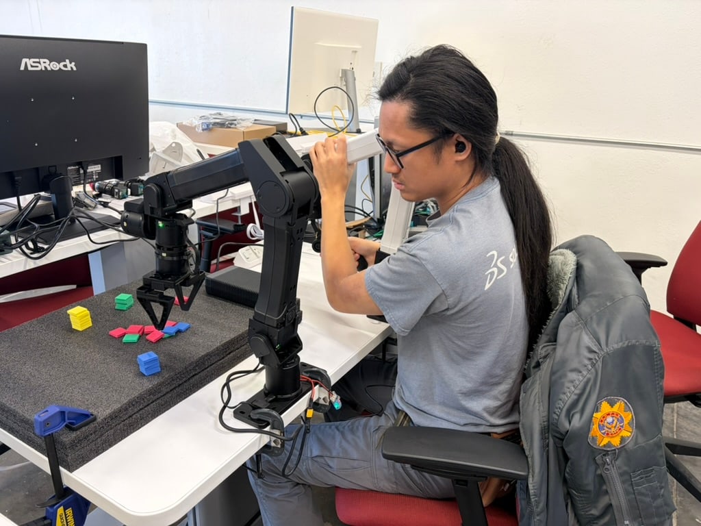 A seated person works with a black mechanical control rig beside a monitor.