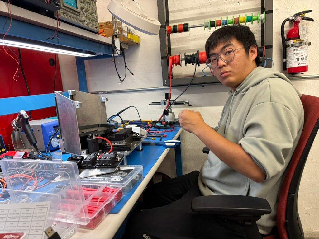 A person works on electronics at a bench filled with wires and components.