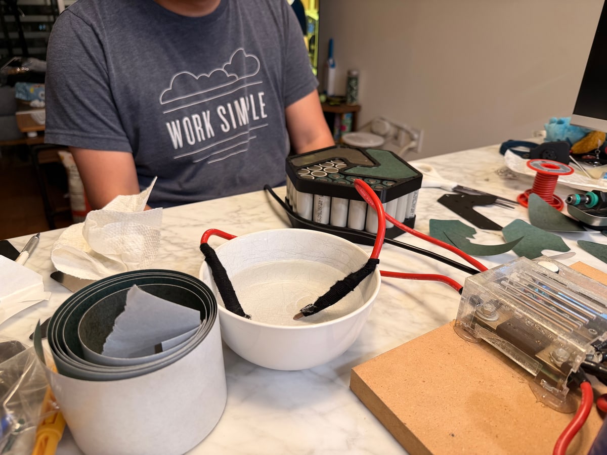 A battery pack, heavy cables, tools, and insulating materials cover a worktable.