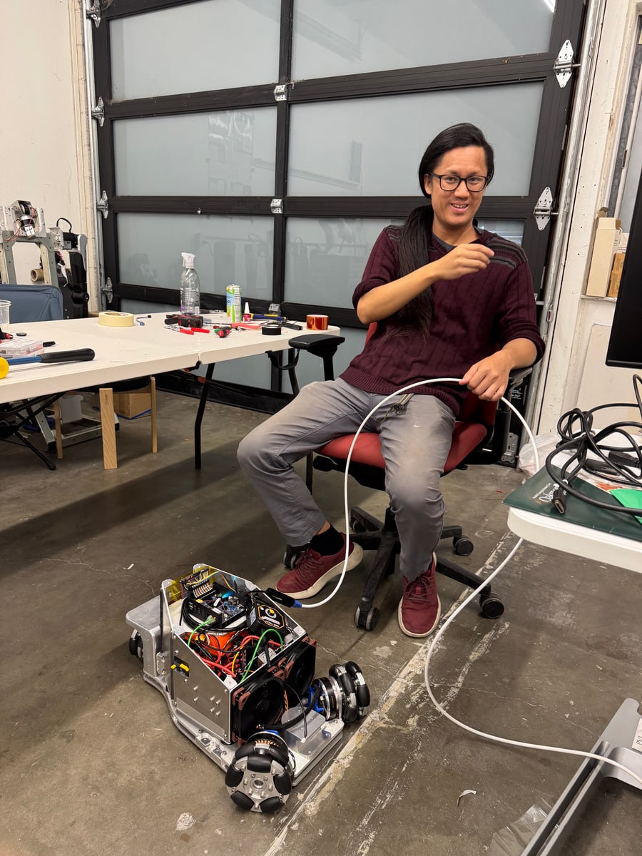 A person sits beside an exposed wheeled robot base in the workshop.
