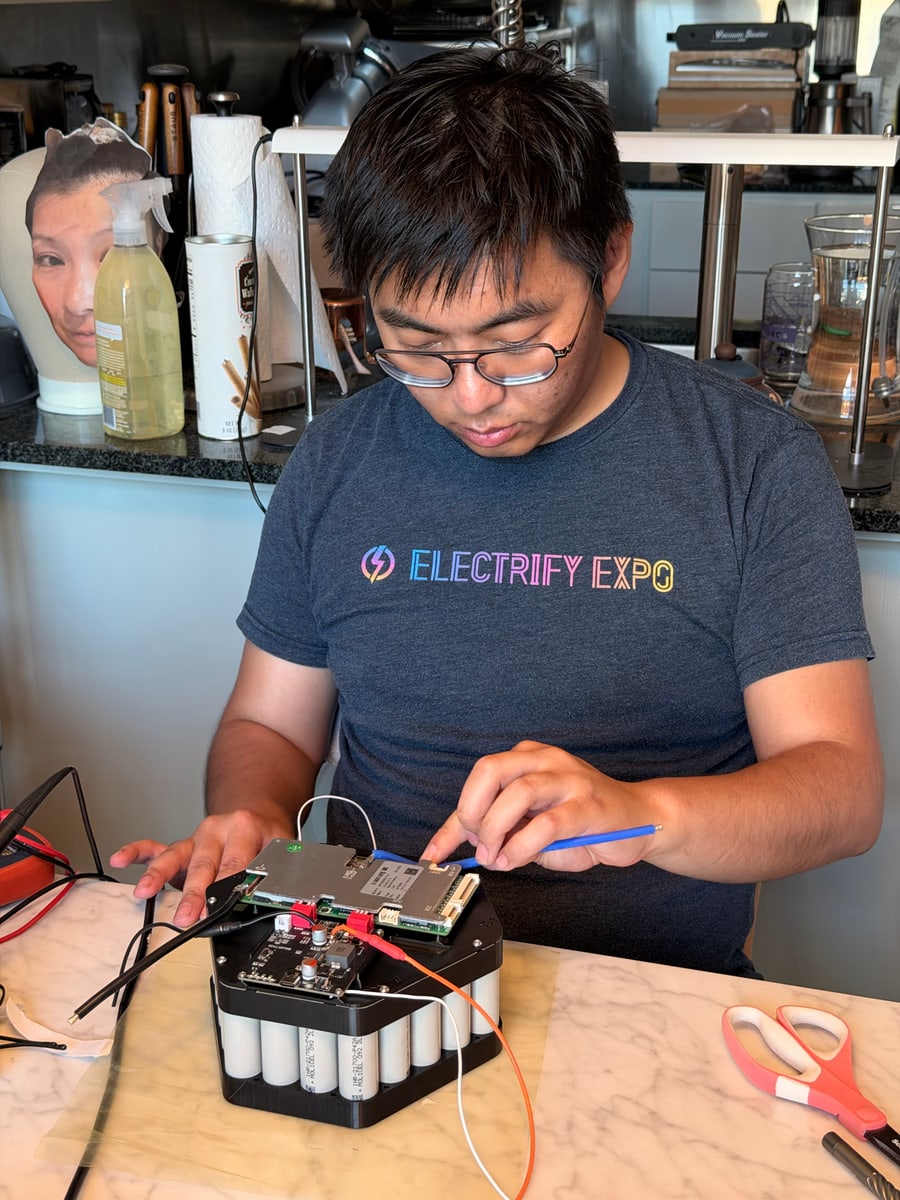 A person works on a battery pack and circuit boards at a table.