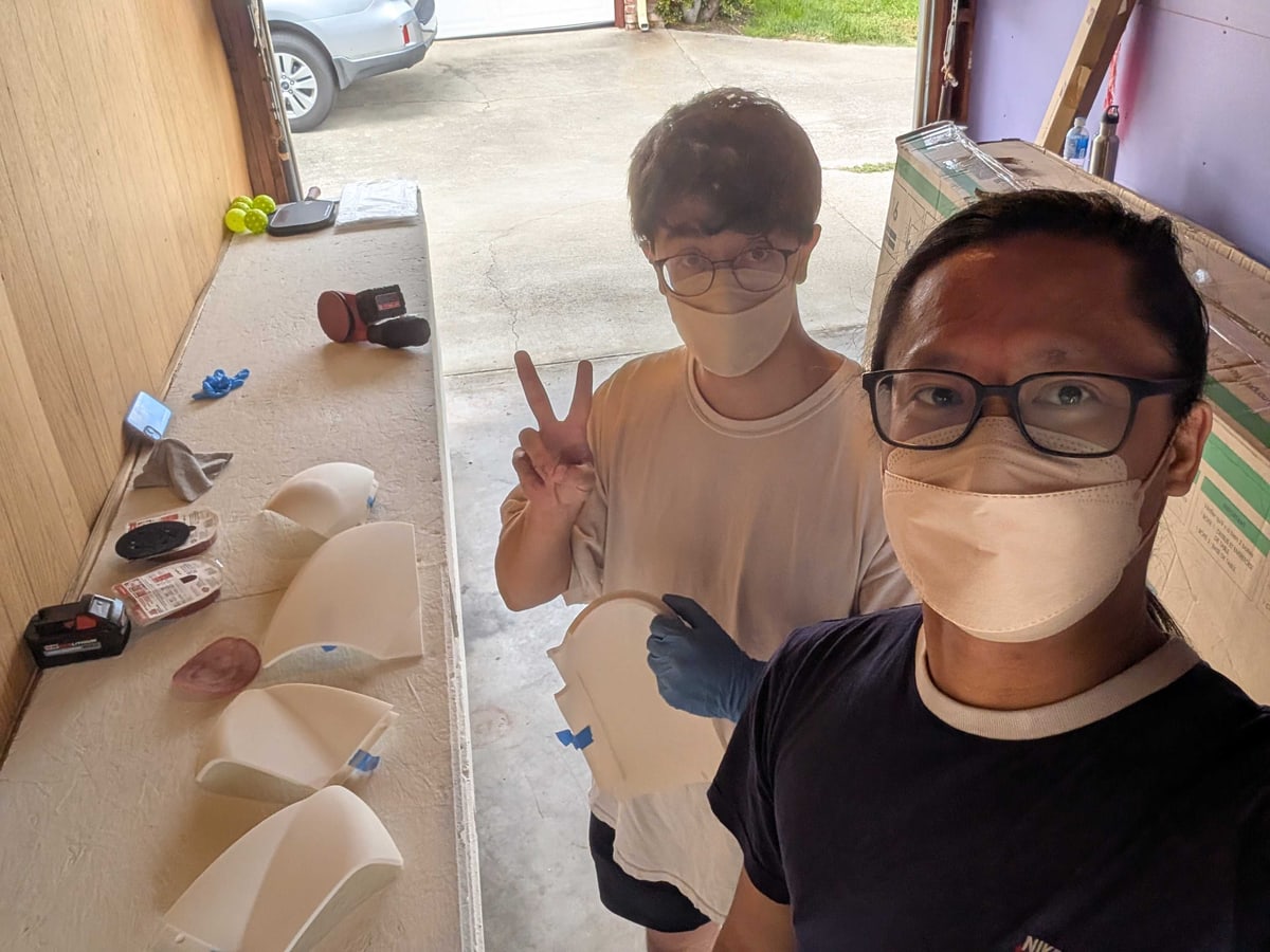 Two masked people pose beside white robot shells.