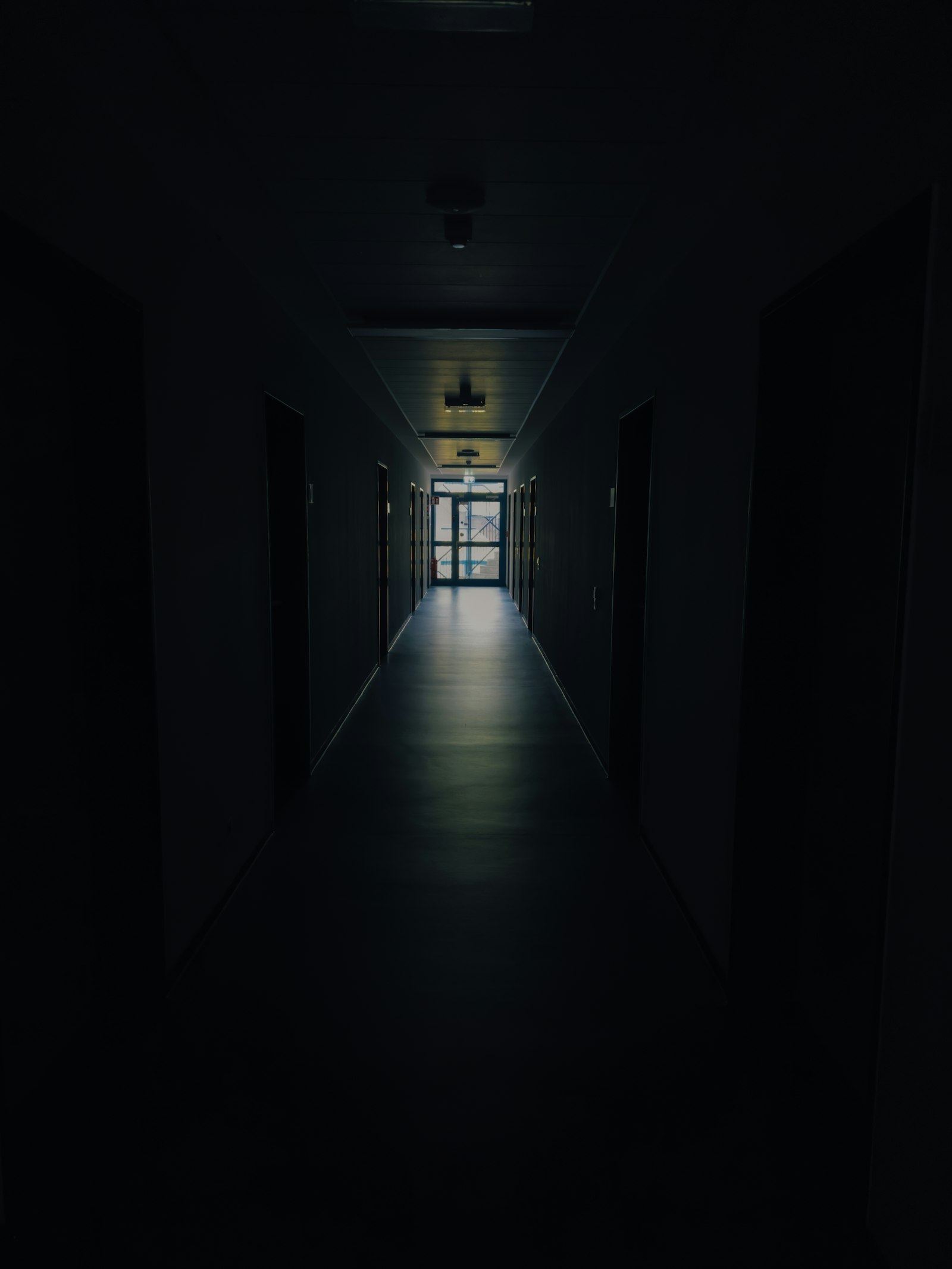 An empty hallway at night, lined with doors, leading to a distant lit exit
