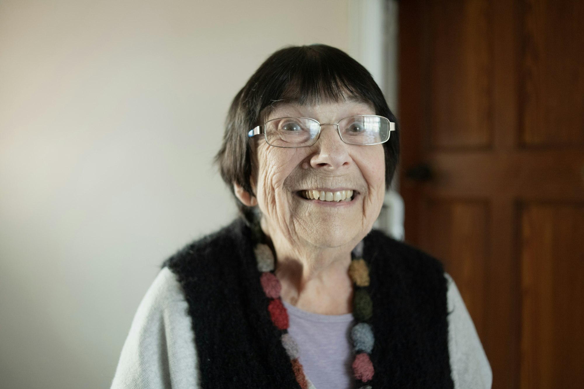 An older woman with glasses and a necklace, smiling warmly